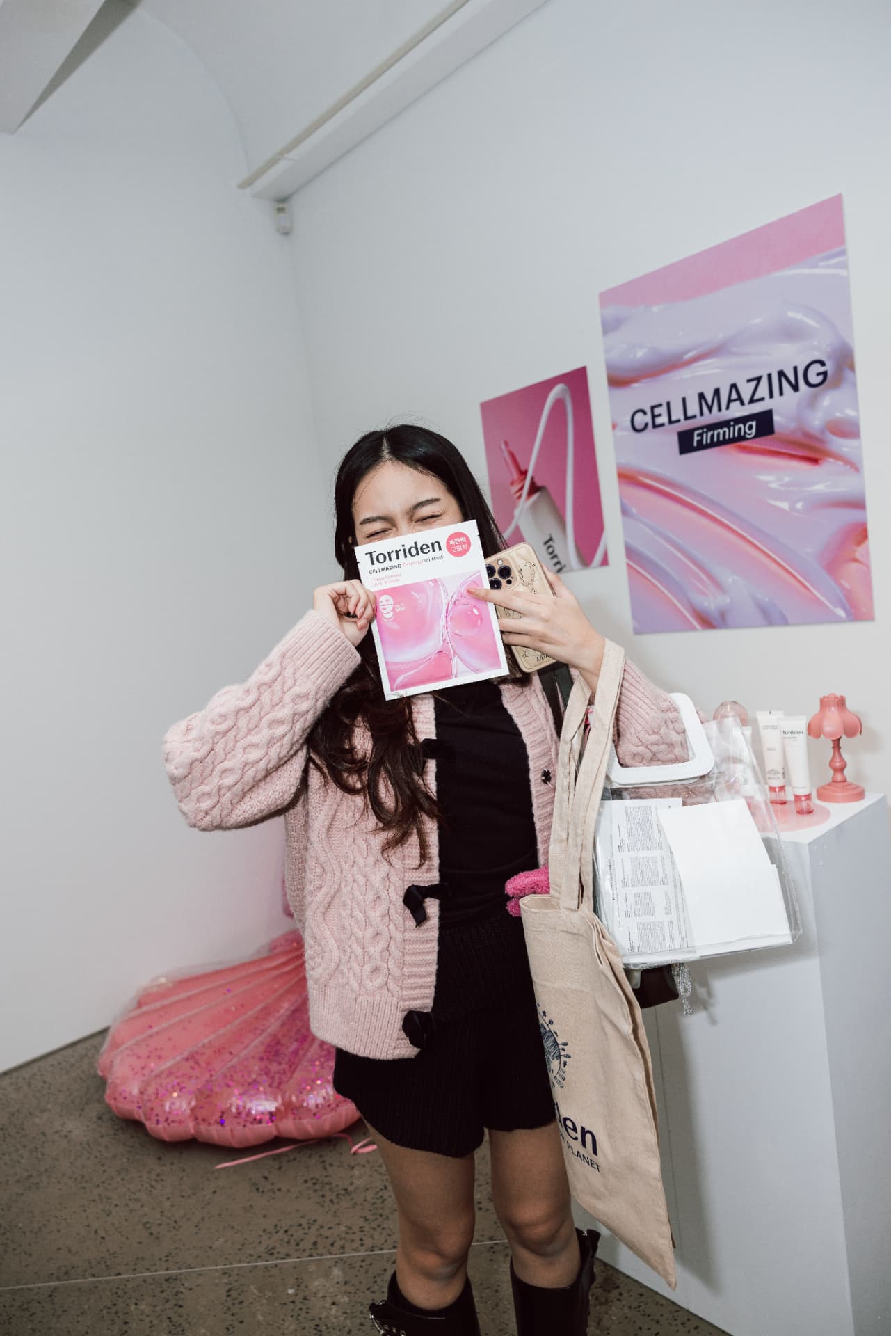 Attendee holding a Torriden Cellmazing Firming mask beside the pink Cellmazing poster wall